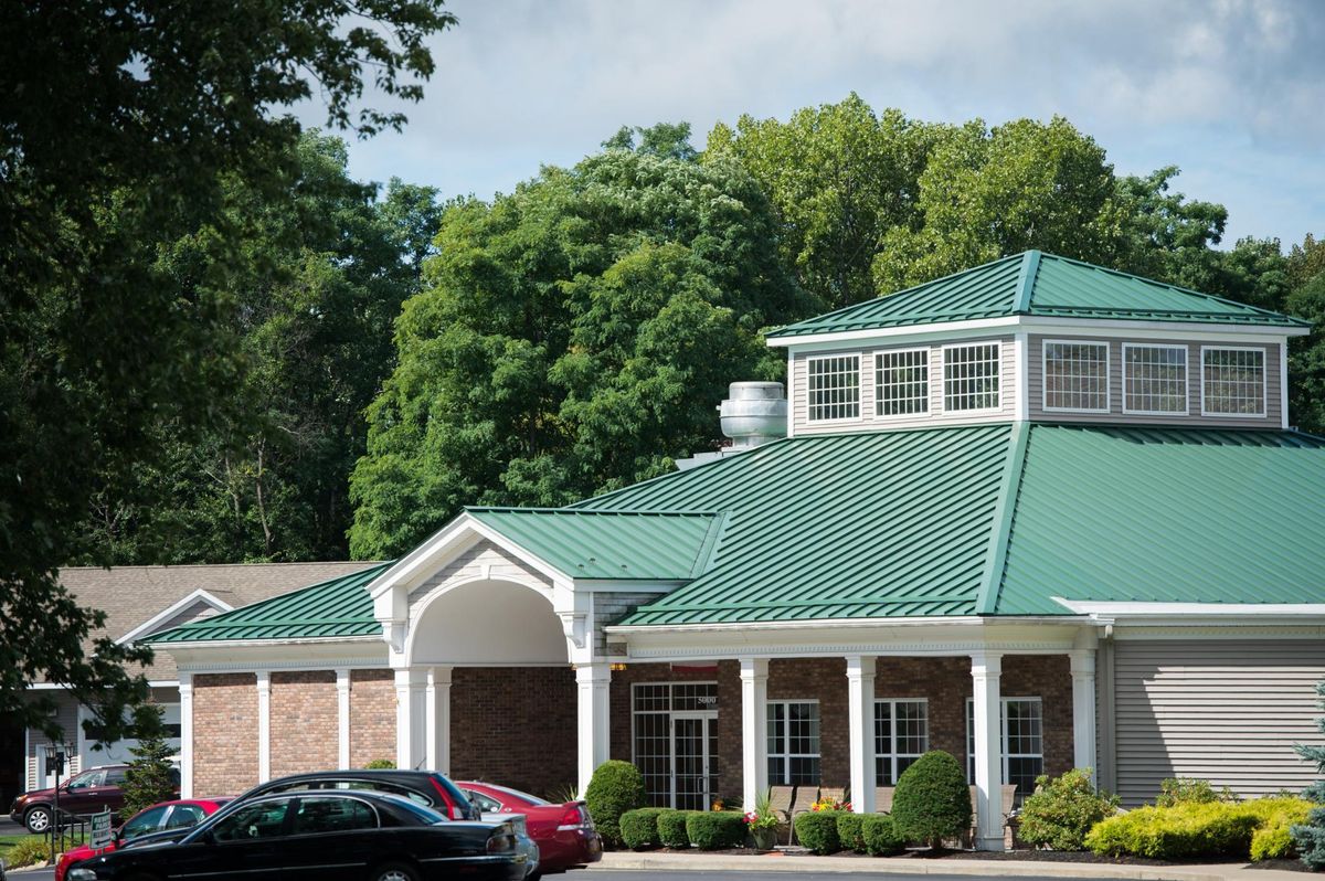A building with a green roof and white columns, surrounded by trees, with cars parked in front.