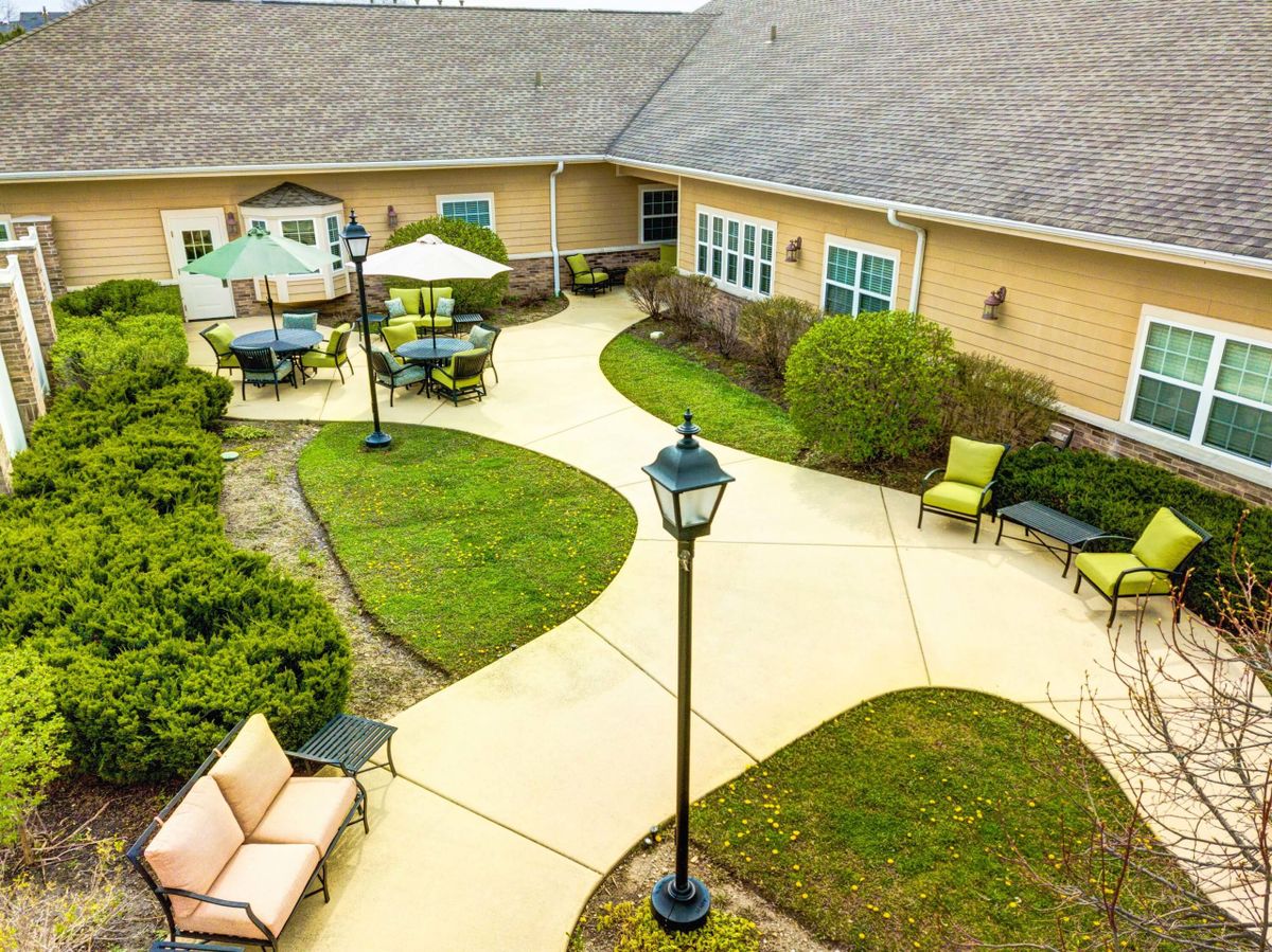 A view of a courtyard with pathways and outdoor seating areas, surrounded by greenery and a building.