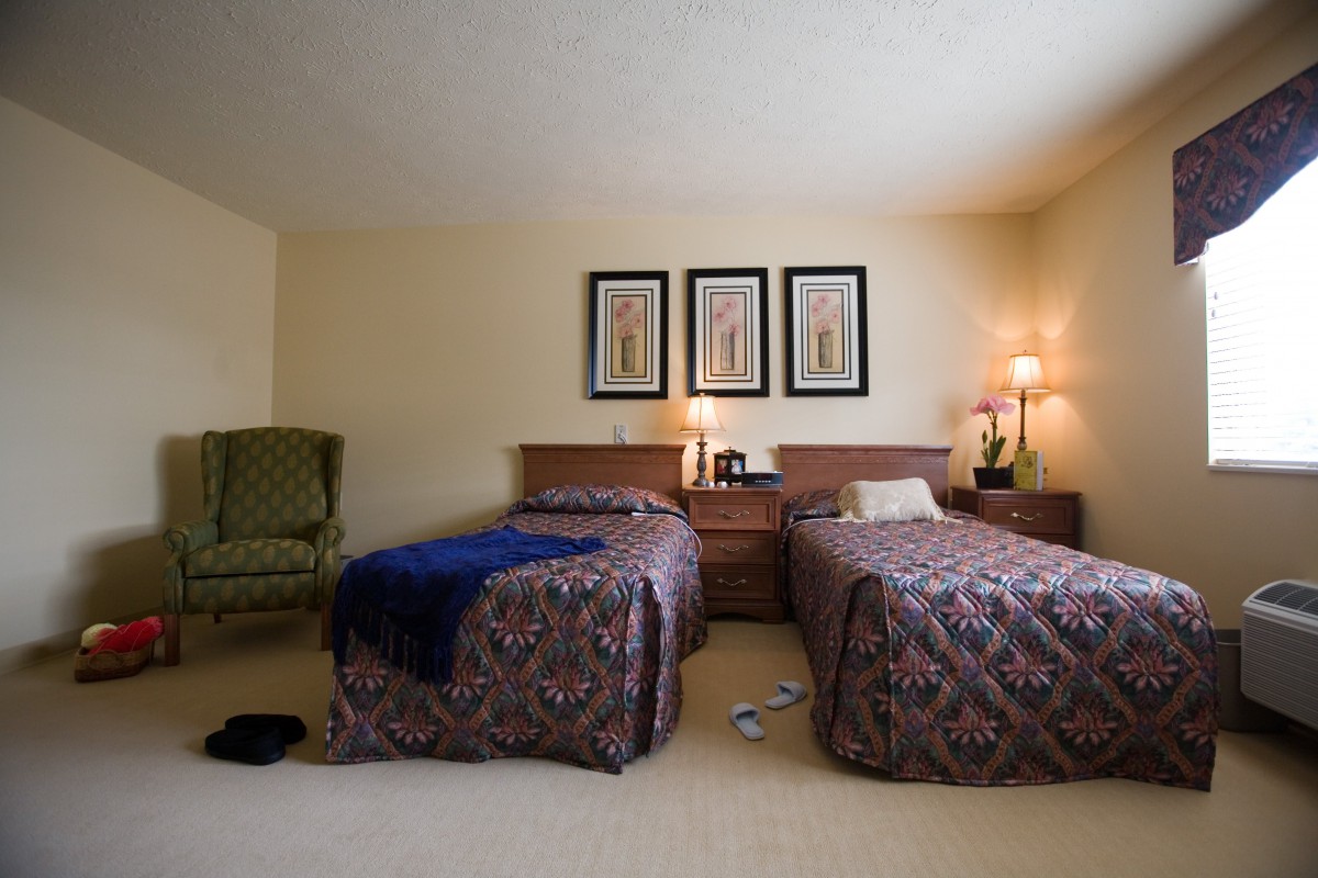 A cozy bedroom with twin beds, a nightstand, decorative artwork, and a comfortable chair.