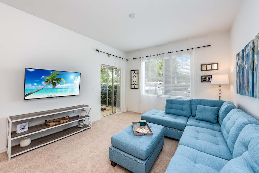 A bright and modern living room featuring a blue sectional sofa, television, and abundant natural light.