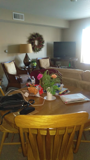 A cozy living room featuring a wooden table adorned with flowers and various items, complemented by comfortable seating and a television.