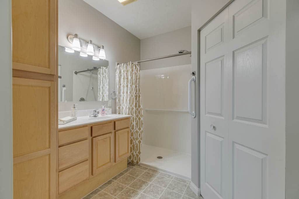 A well-lit bathroom featuring a shower with a curtain, a vanity with a mirror, and wooden cabinets.