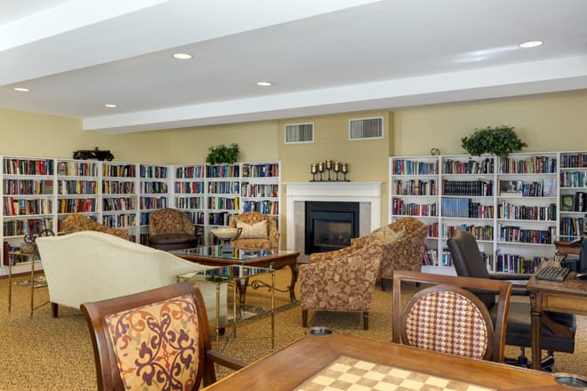A cozy library with bookshelves, comfortable seating, and a fireplace.