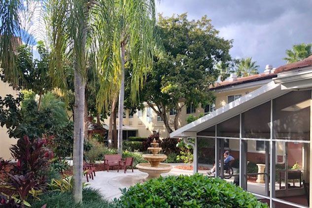 A serene garden patio featuring a fountain and surrounded by lush palm trees.