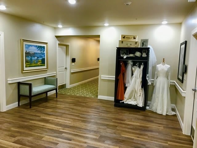 An interior hallway with wedding dresses displayed on a mannequin and shelf, complemented by artwork and seating.