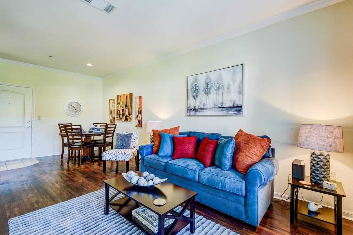 A cozy living room with a blue sofa adorned with colorful cushions, adjacent to a dining area.