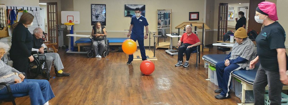 A healthcare professional assists elderly individuals in a physical therapy session using exercise balls.