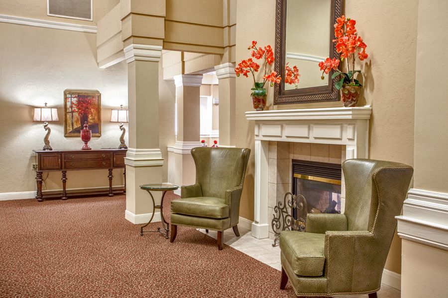 A cozy living room with green armchairs, a fireplace, and vibrant flower decorations.