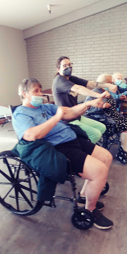 A group of individuals in wheelchairs participate in a seated exercise session while wearing masks.
