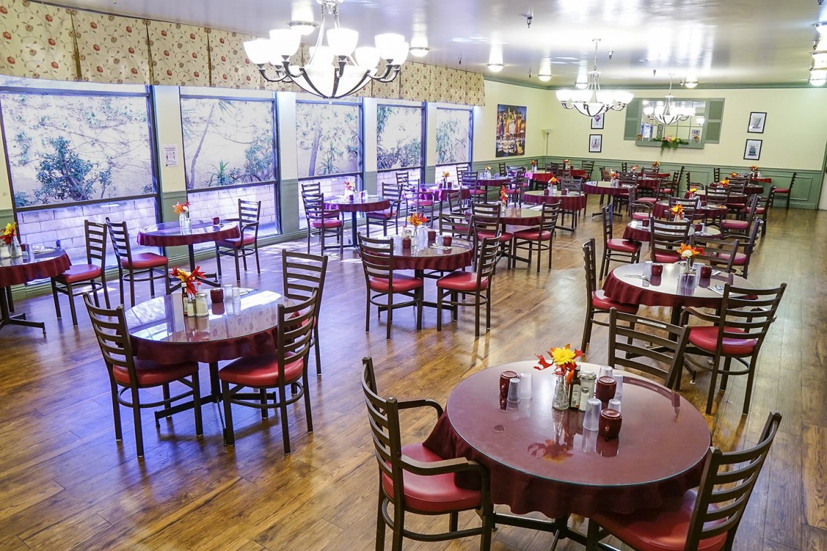 An empty restaurant dining area with neatly arranged tables and chairs, elegant lighting, and decorative elements.
