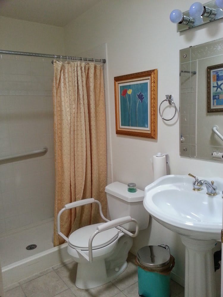 A bathroom with a walk-in shower, beige shower curtain, pedestal sink, and framed artwork on the wall.