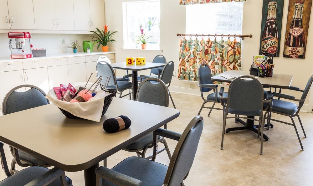 A cozy dining area with multiple tables and chairs, decorated with plants and floral curtains.