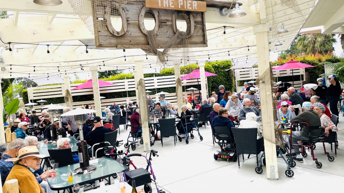 A lively outdoor cafe setting with people enjoying their meals and conversations under a shaded patio.