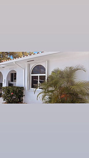 A view of a modern house featuring an elegant arched window and lush palm greenery.