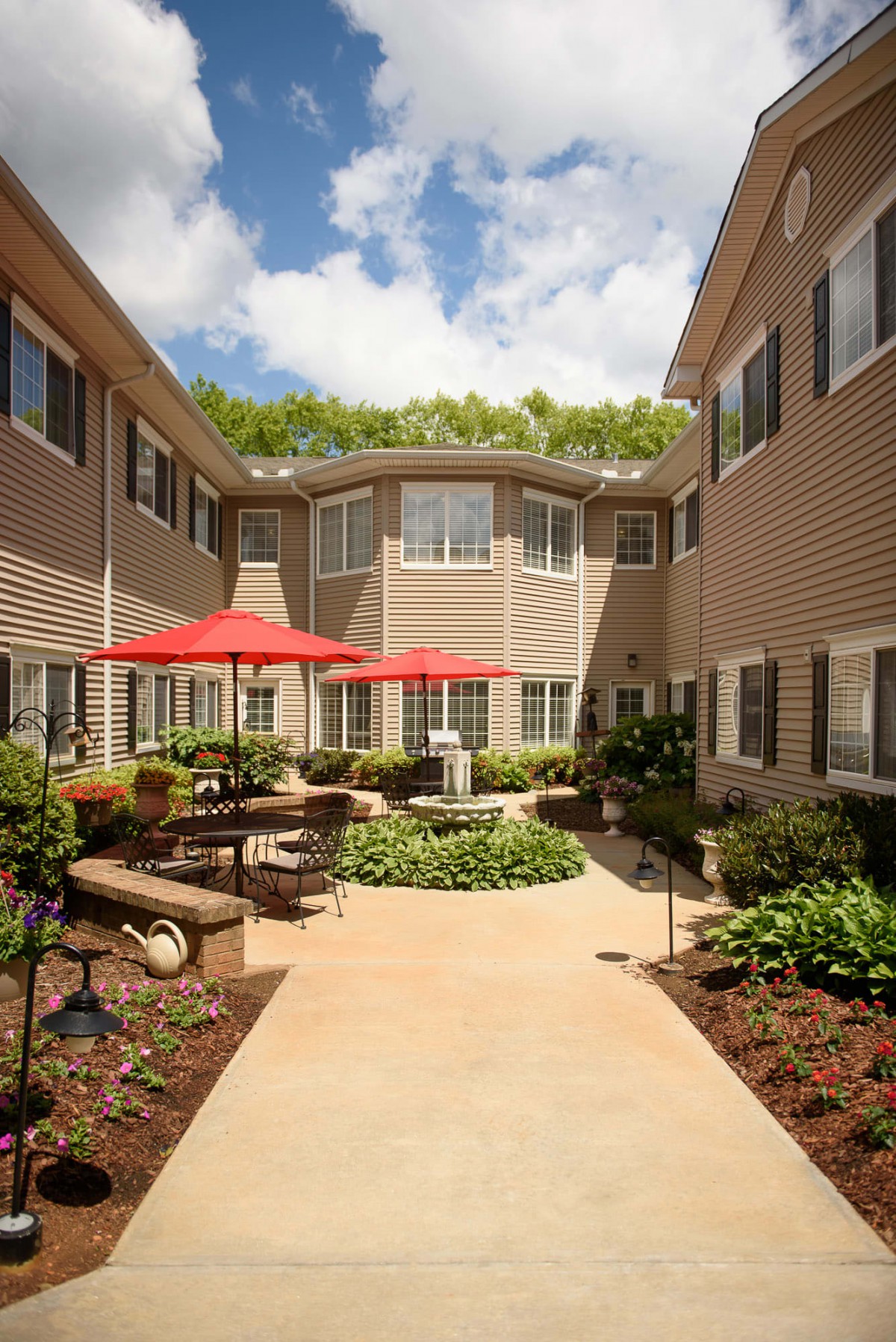 A well-maintained courtyard with outdoor seating and red umbrellas, surrounded by residential buildings on a sunny day.