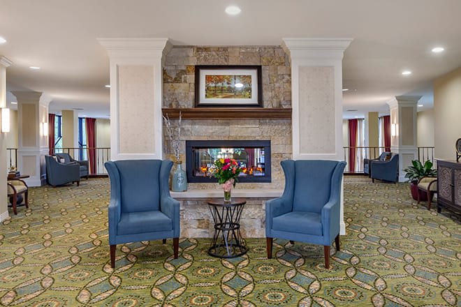A cozy seating area with two blue chairs flanking a fireplace in a well-decorated lobby.