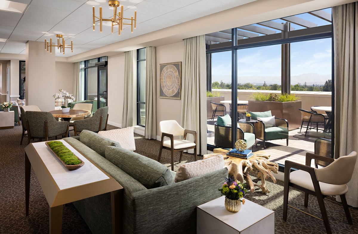 A spacious and luxurious living room with modern furnishings, featuring large windows that open to a balcony with outdoor seating.