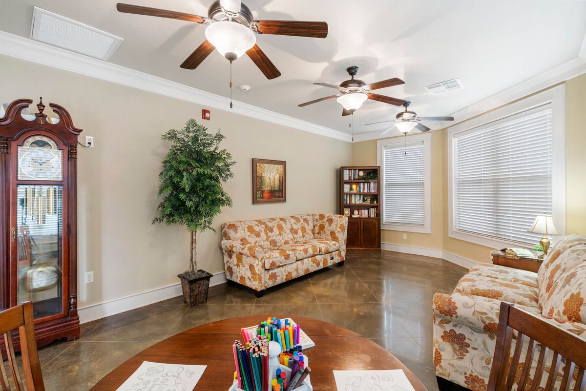 A cozy living room with floral sofas, ceiling fans, and a bookshelf against a hardwood floor.