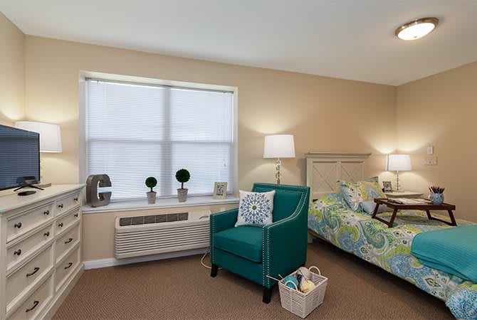 A cozy bedroom with a bed, teal armchair, and decorative elements under soft lighting.