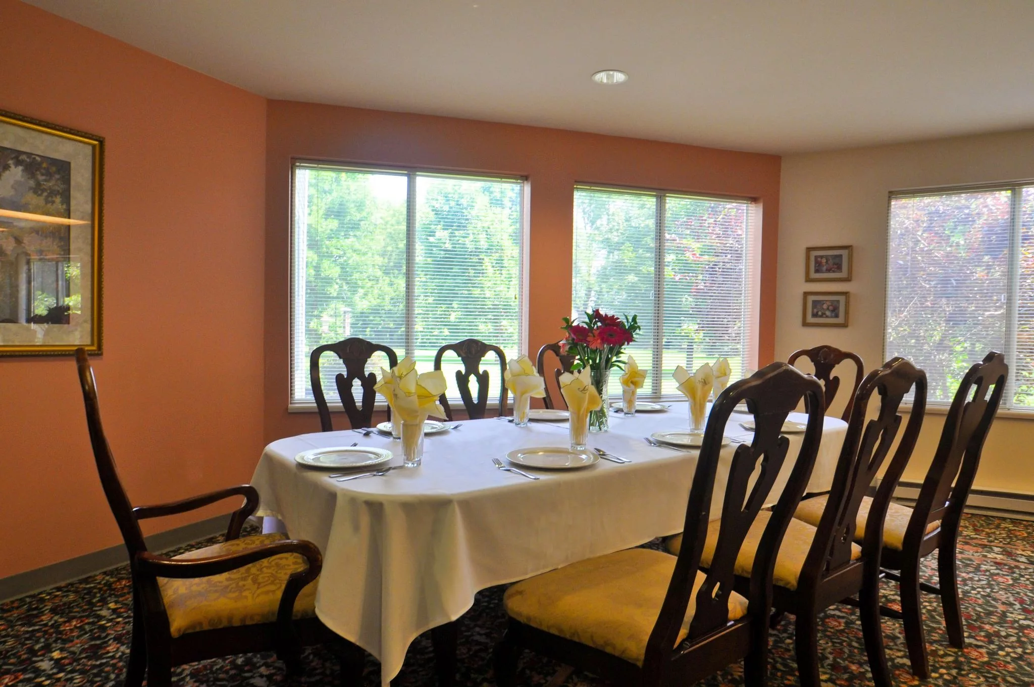 A well-set dining table with yellow napkins and a floral centerpiece in a bright room with large windows.