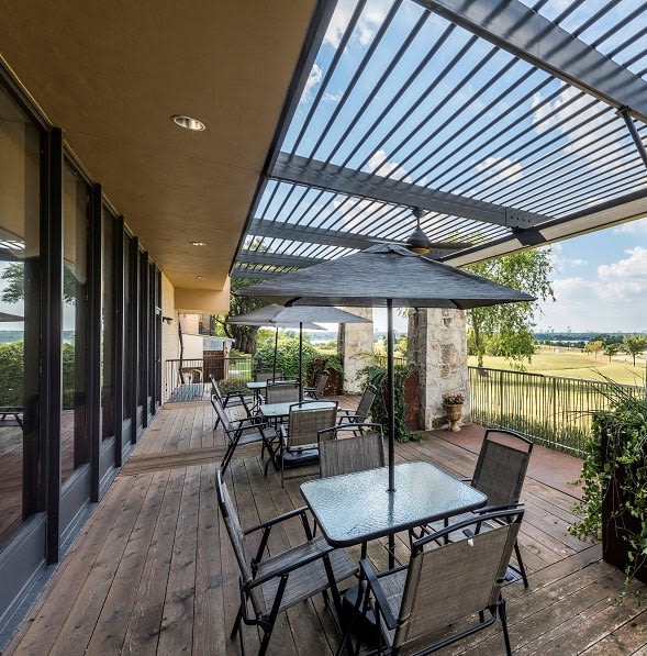A cozy outdoor patio area with tables and chairs under a pergola, offering a scenic view.
