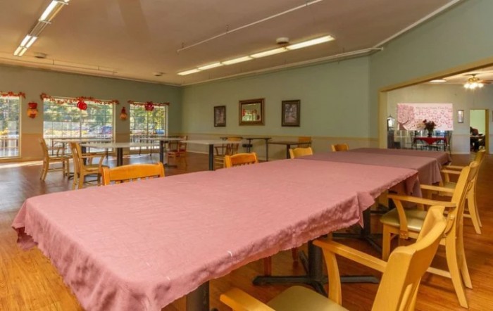 An empty dining room with a long table covered in a pink tablecloth and surrounded by chairs.