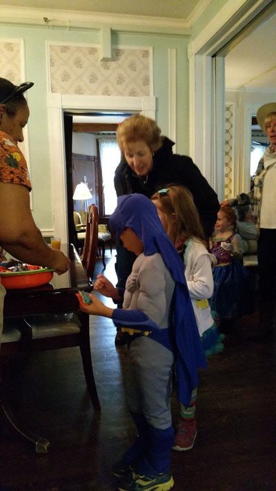 Children in costumes receiving candy indoors during a Halloween celebration.