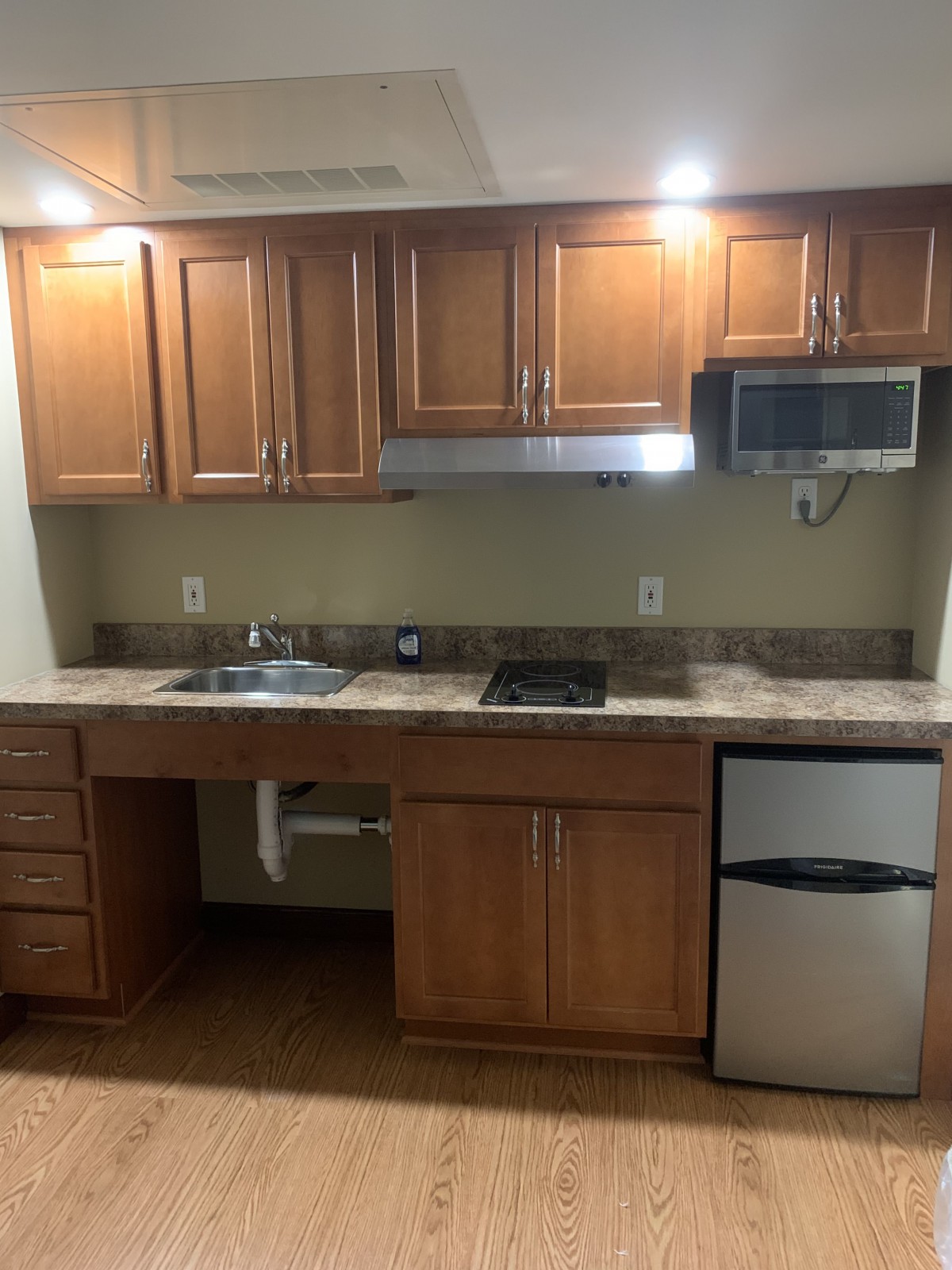 A compact kitchen with wooden cabinets, a sink, microwave, and small refrigerator.