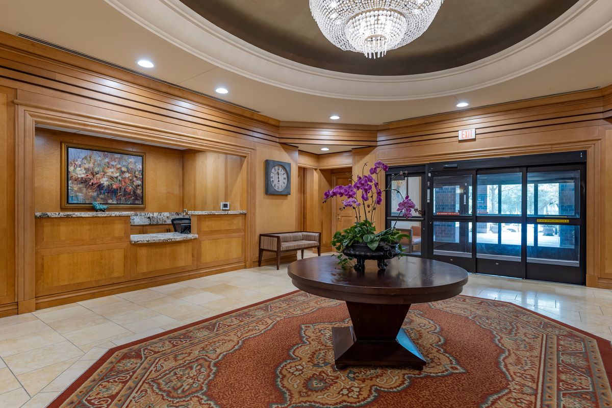 A well-lit hotel lobby featuring a chandelier, a round table with a floral arrangement, and elegant wood paneling.