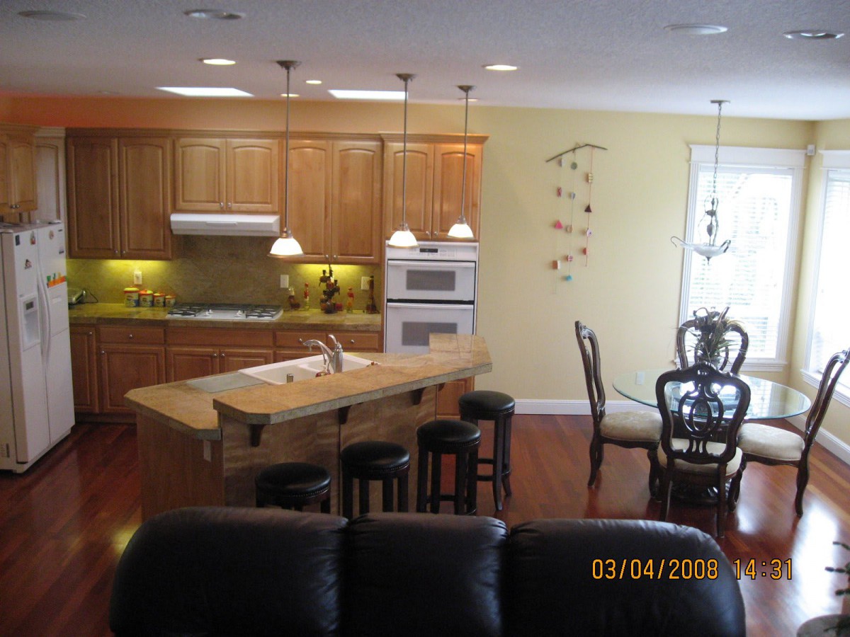 A modern kitchen and dining area featuring wooden cabinets, an island with stools, and pendant lighting.
