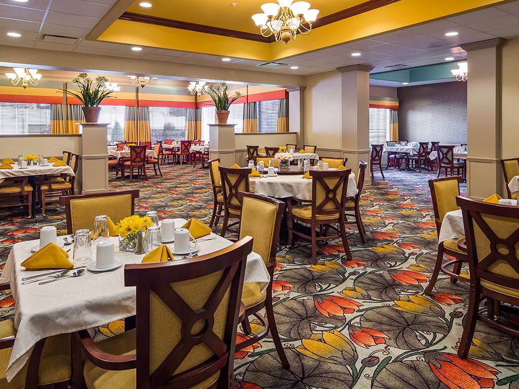 A well-decorated dining area with neatly arranged tables and chairs, featuring a colorful carpet and chandelier.