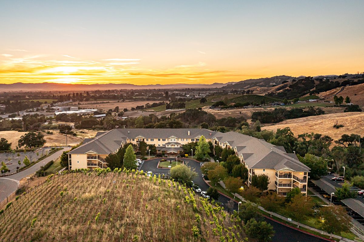 A scenic aerial view of a vineyard with a building nestled among rolling hills at sunset.