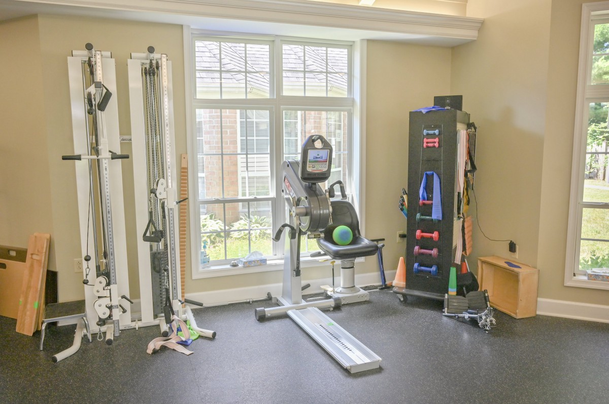 A well-equipped home gym with various exercise machines and weights in a brightly lit room.