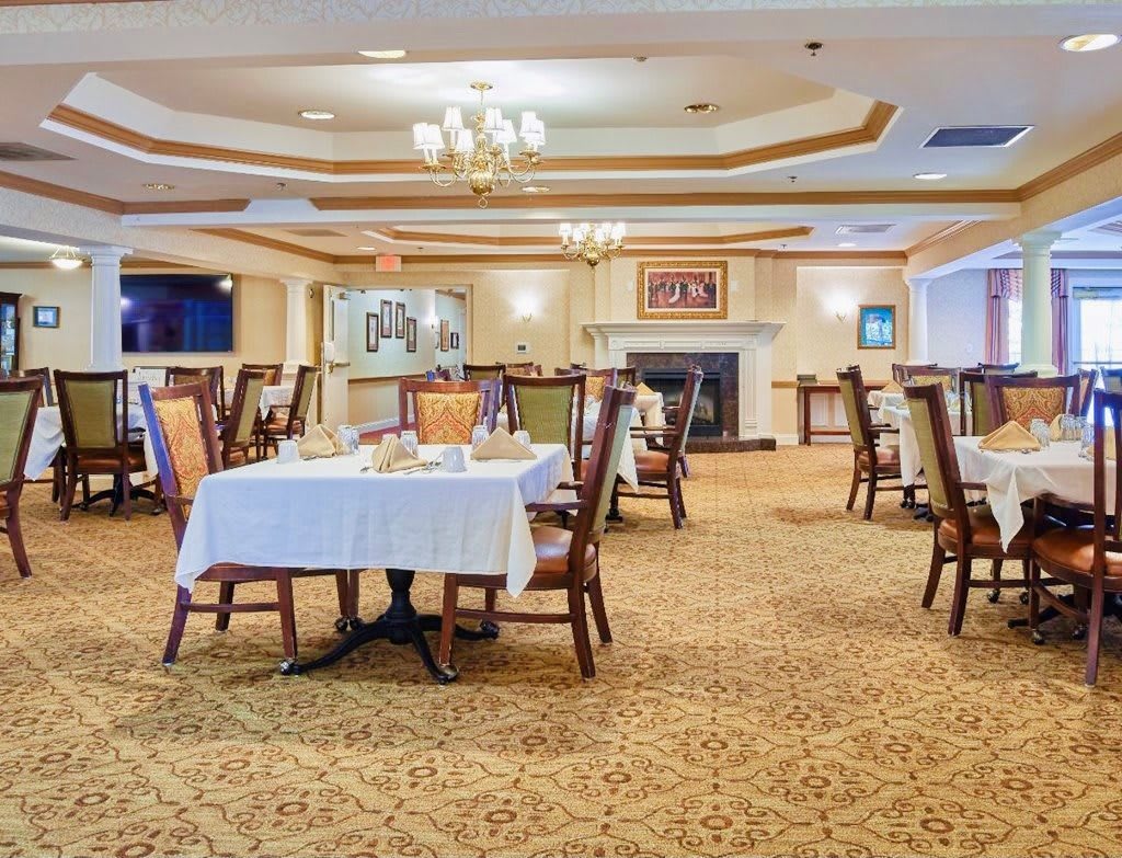 A spacious restaurant dining area with arranged tables and chairs, a chandelier overhead, and a cozy fireplace.