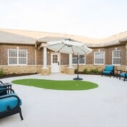 A spacious outdoor courtyard with seating and an umbrella in front of a brick building.