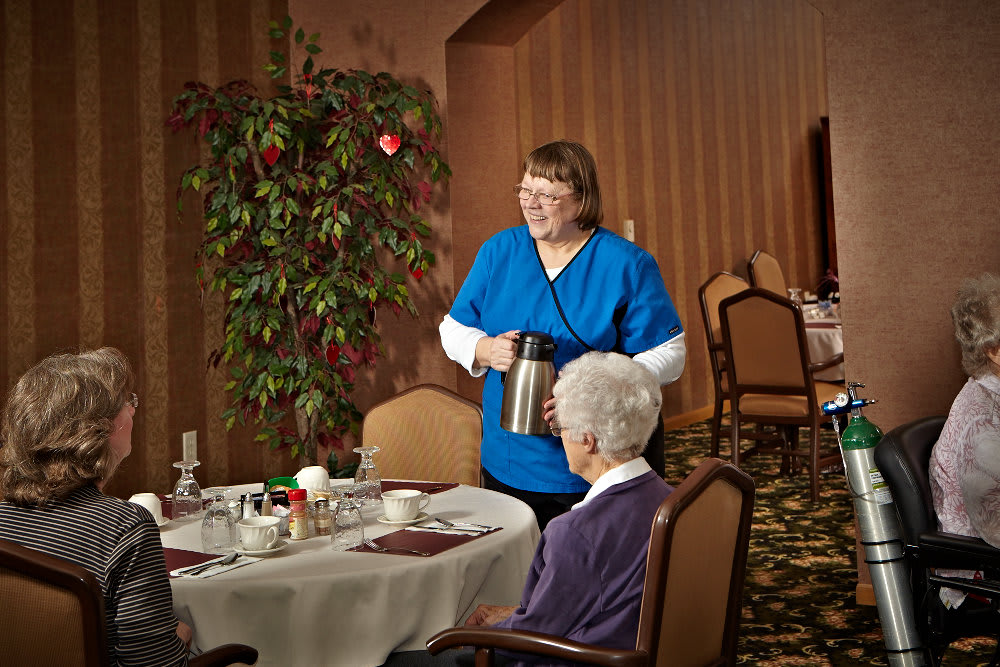 A caregiver serving a meal to an elderly woman in a dining room setting.