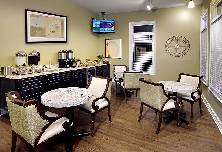 A cozy seating area with tables and chairs, featuring a coffee station and a wall-mounted television.
