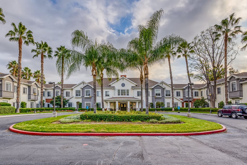 A large building with an elegant entrance, surrounded by palm trees and landscaped greenery under a partly cloudy sky.