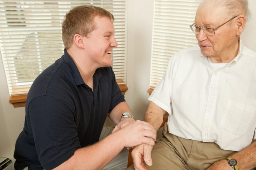 A younger person engaging in a friendly conversation with an elderly man in a home setting.