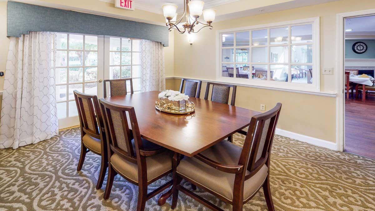 A well-lit dining or meeting room with a wooden table and chairs arranged neatly around it.