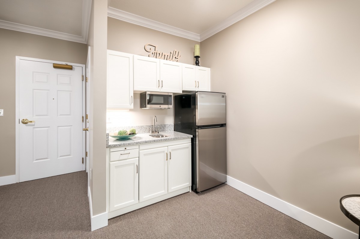 Compact kitchenette with white cabinetry and stainless steel appliances.