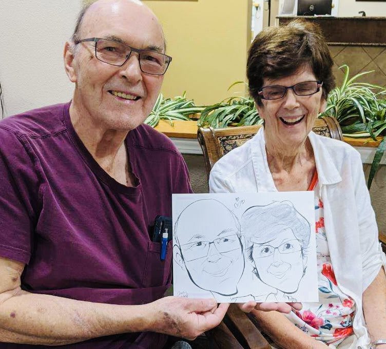 Elderly couple smiling and holding a drawing of themselves.