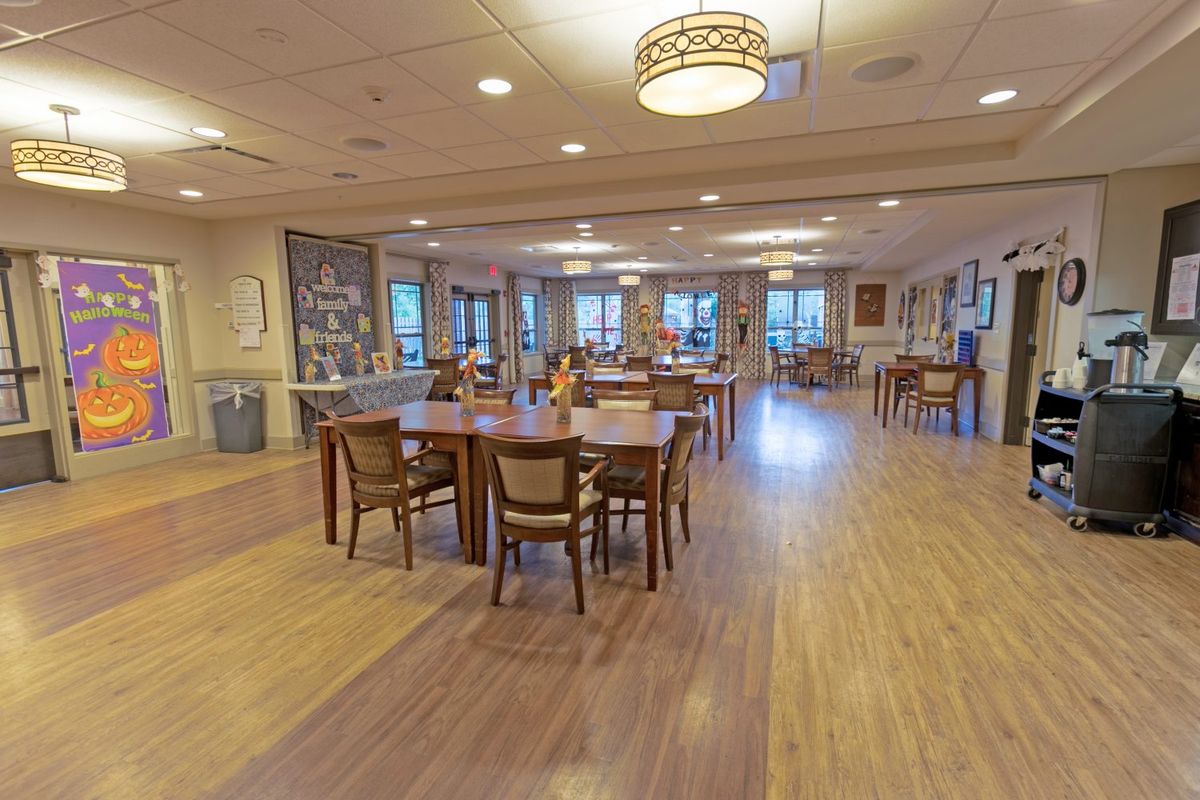 An empty dining room with wooden floors and neatly arranged tables and chairs.