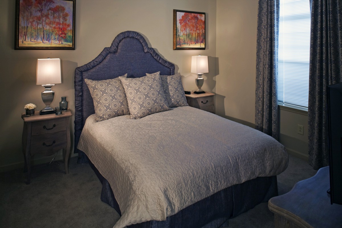 A cozy bedroom with a neatly made bed, illuminated by bedside lamps and decorated with artwork on the walls.