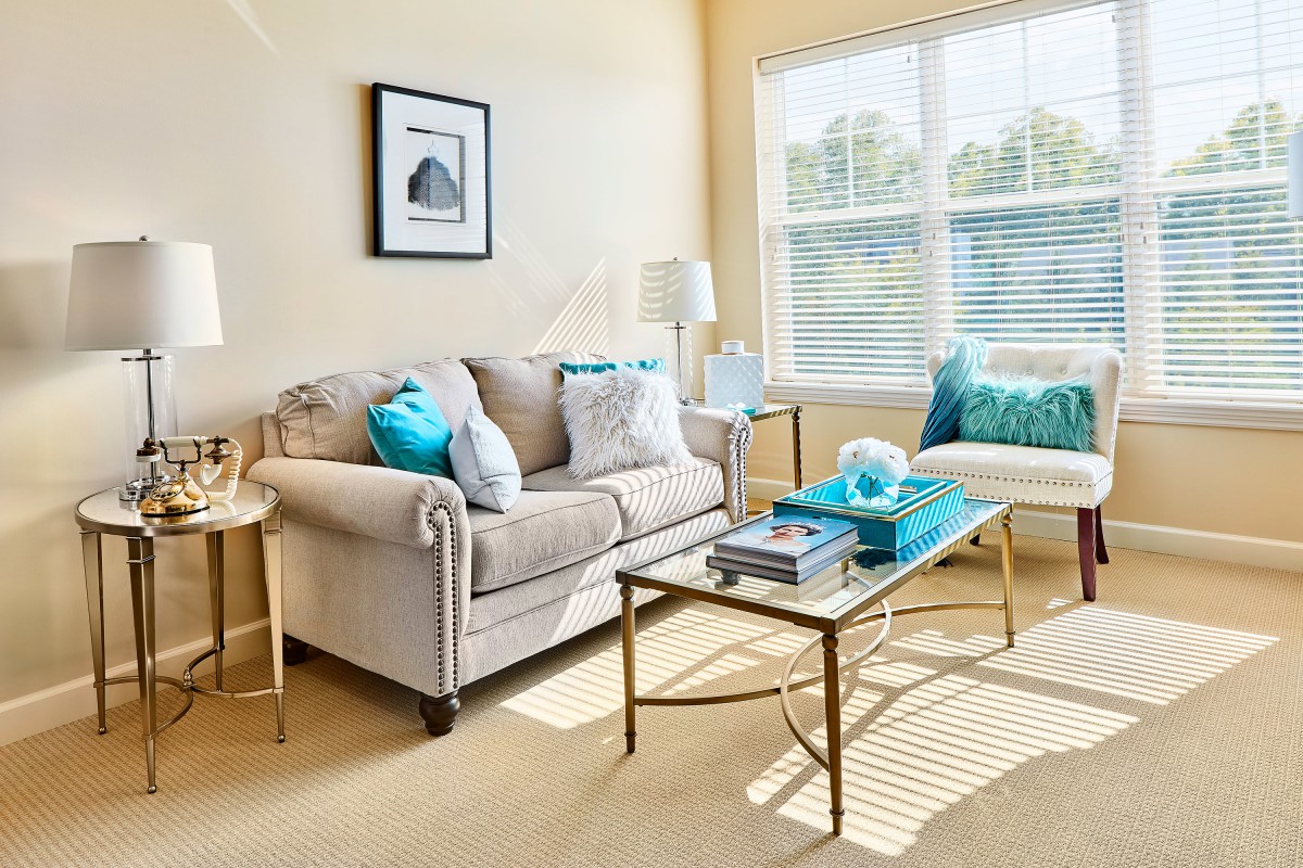 A bright and cozy living room with a beige sofa, colorful cushions, and a glass coffee table.