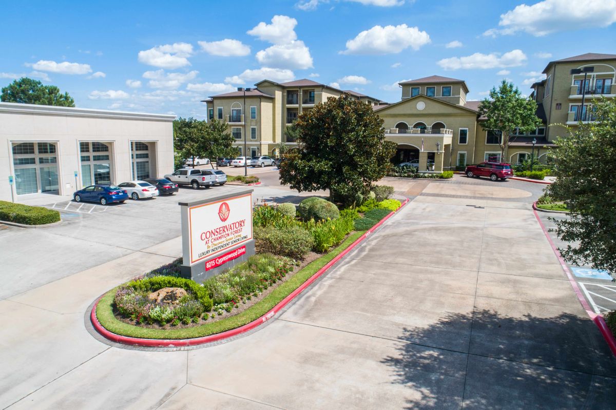 A hotel building with a landscaped entrance and parking lot under a blue sky with clouds.