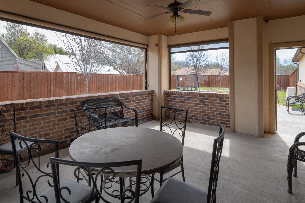 A cozy screened patio with a round table and metal chairs, surrounded by brick walls and overlooking a fenced yard.