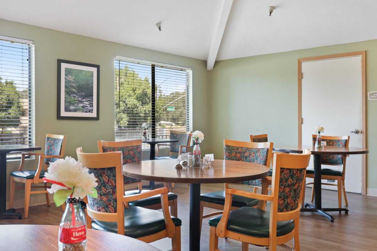 A cozy dining area with wooden tables and chairs, decorated with flowers and natural light filtering through the windows.