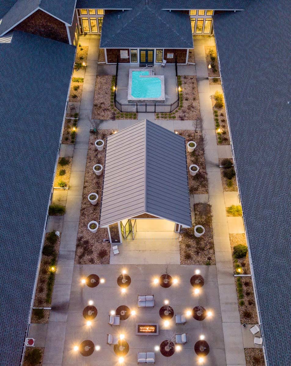 A beautifully lit rooftop area with a pool and seating, viewed from above during the evening.