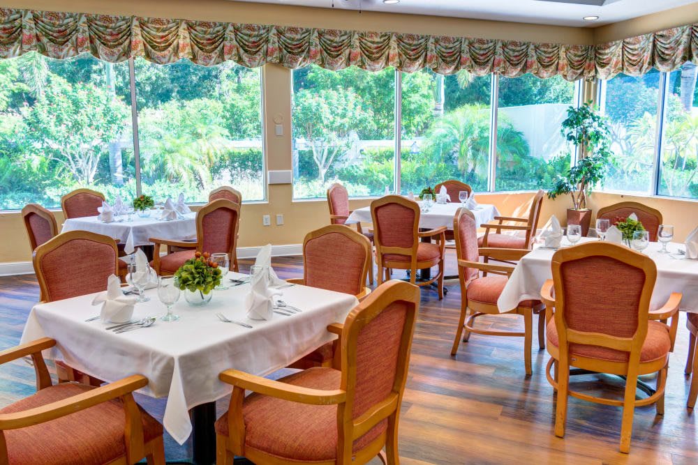 A well-lit dining area with elegantly set tables and comfortable chairs, offering a view of the greenery outside.
